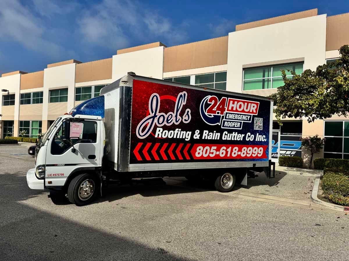 White box truck with Joes Roofing & Rain Gutter 24 Hour service parked outside a commercial building