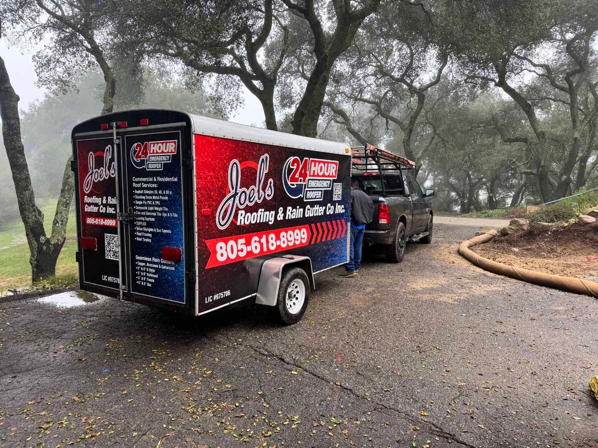 Black trailer with colorful ads parked on a wet, tree-lined road behind a pickup truck