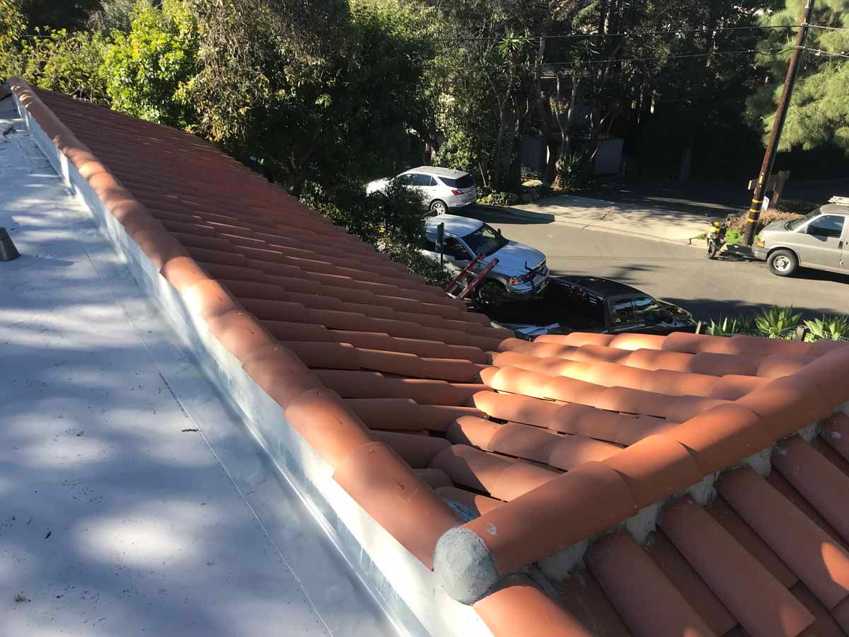 Red-tiled roof corner overlooking parked cars and trees in a sunny lot