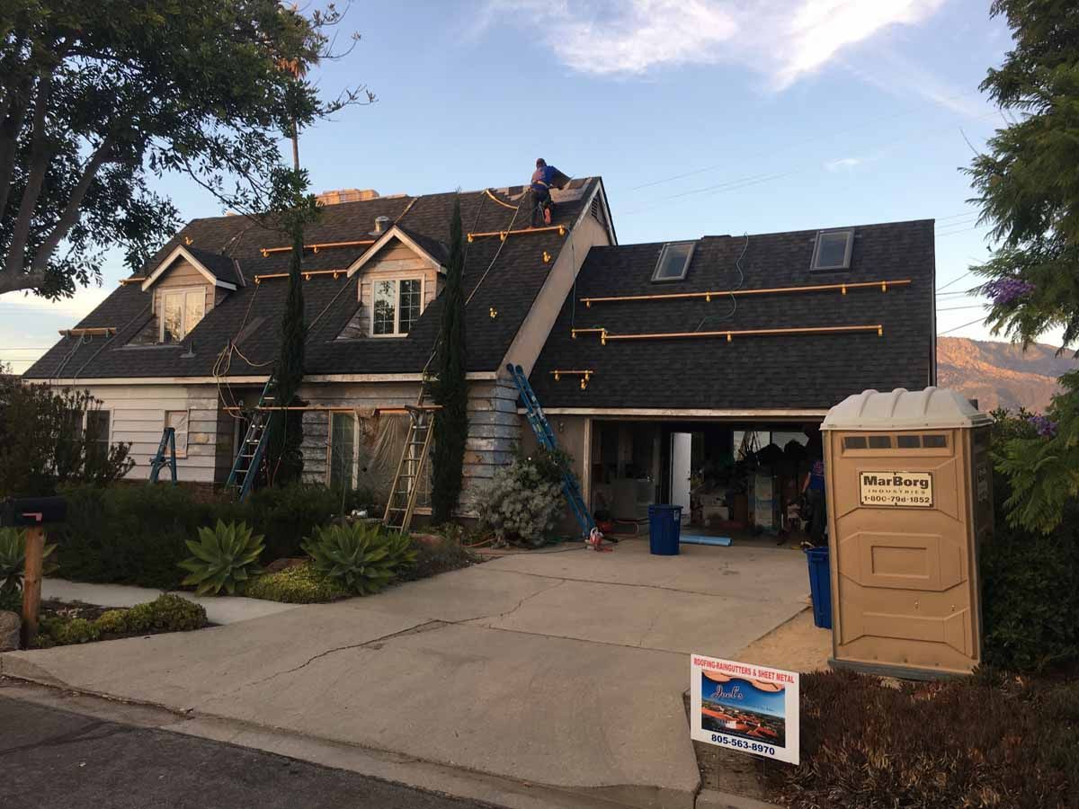 House exterior with steep dark roof, driveway, and a portable toilet in the foreground