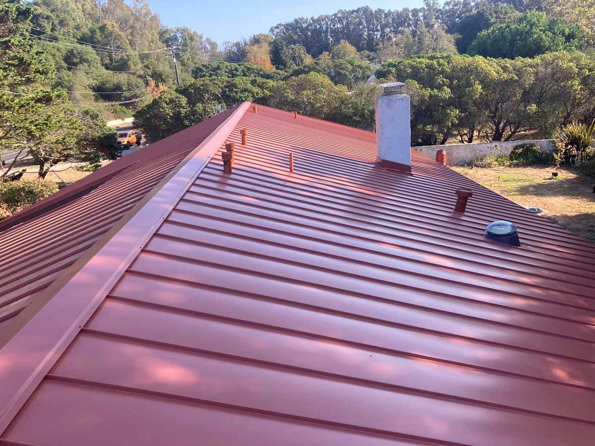 Red metal roof with chimney, surrounded by trees and hills in daylight