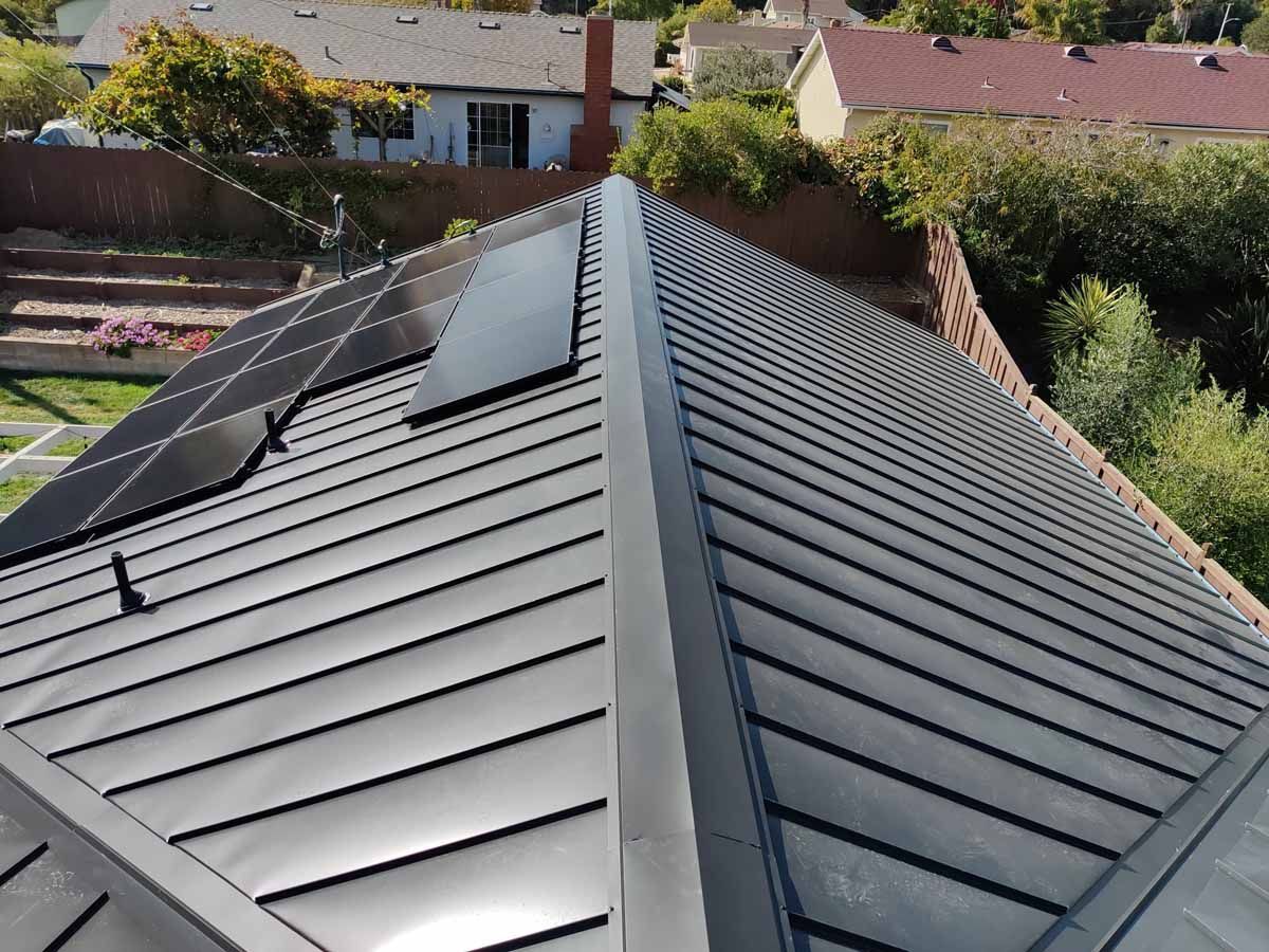 Metal roof with solar panels on a house, viewed from above in a suburban neighborhood