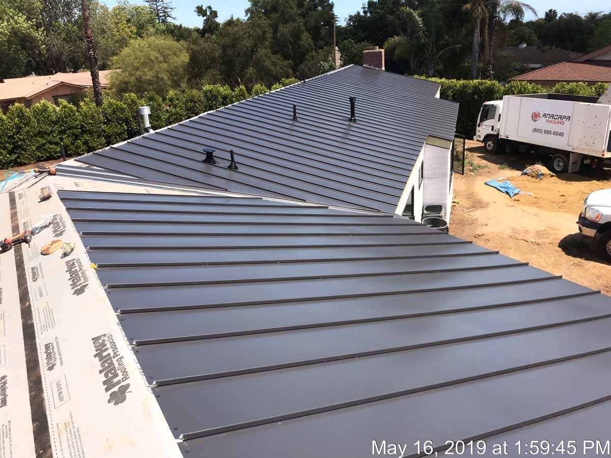 Long black metal roof under construction beside trees and a work truck