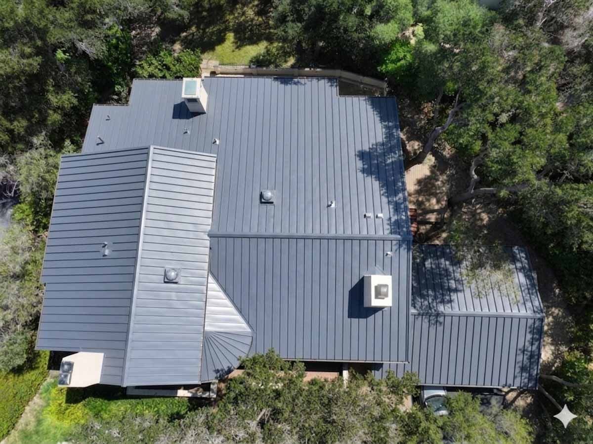 Aerial view of a gray metal-roof house surrounded by dense green trees.