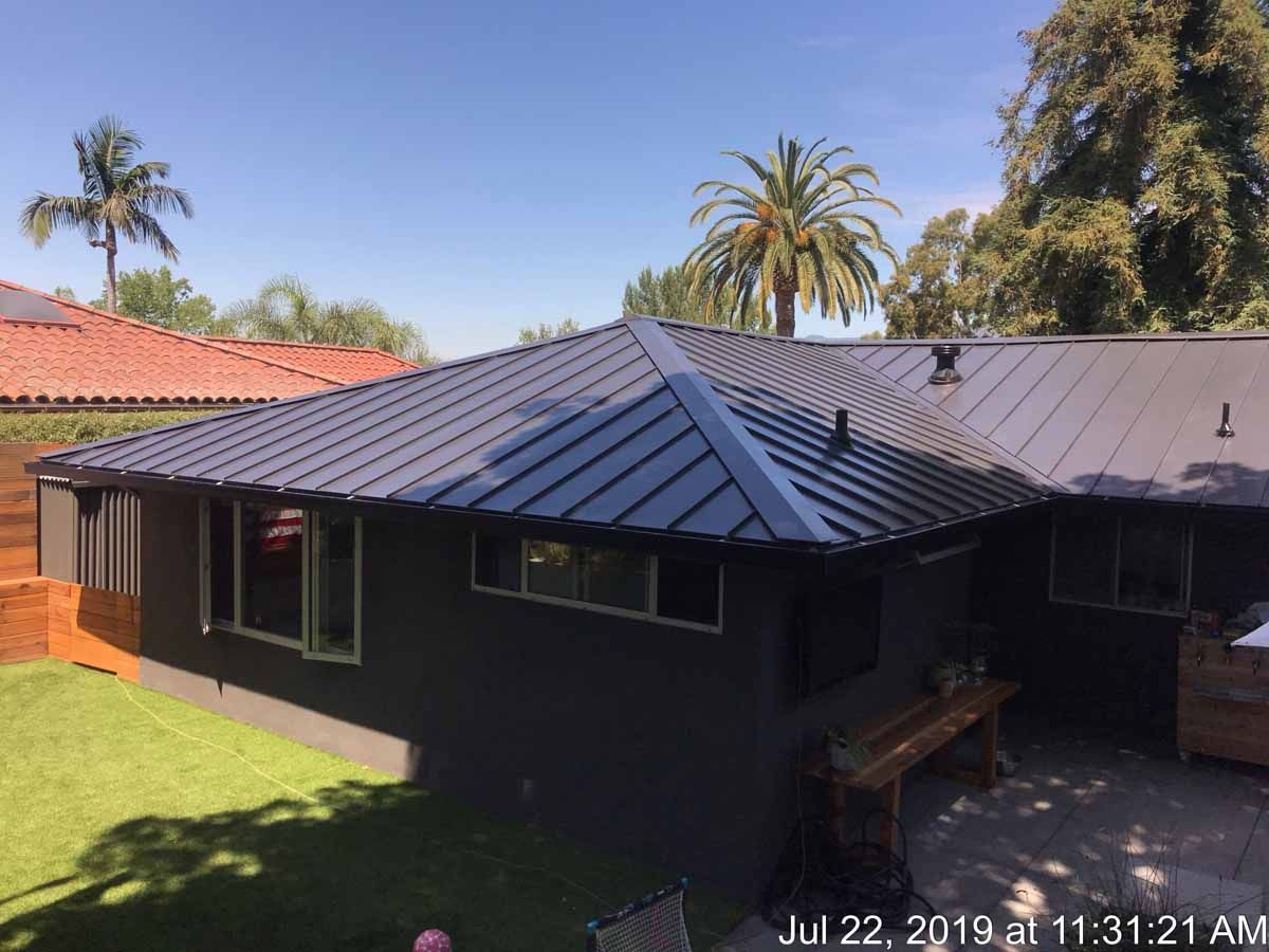 Dark gray house with a metal roof and backyard lawn under a clear blue sky