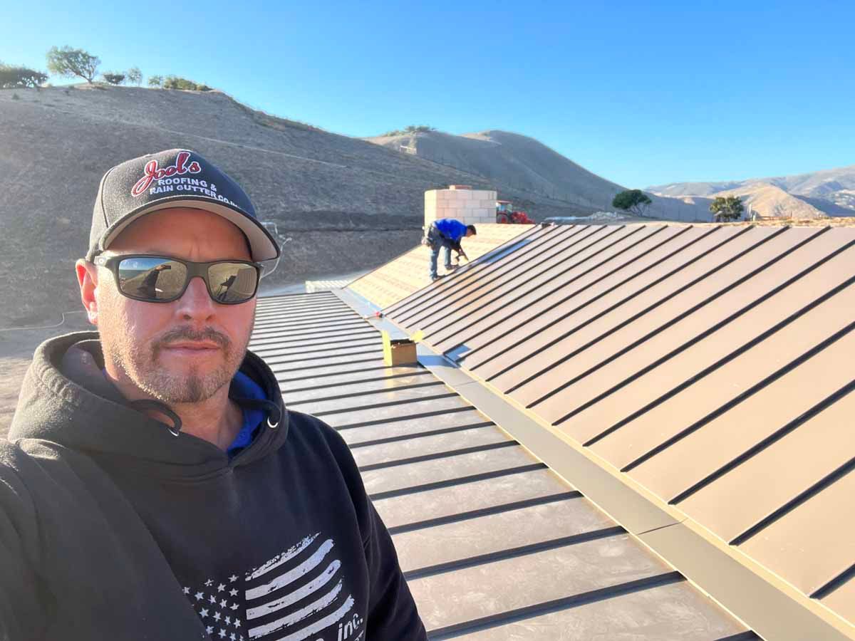 Man on a rooftop with solar panels, wearing sunglasses and a cap, with hills in the background