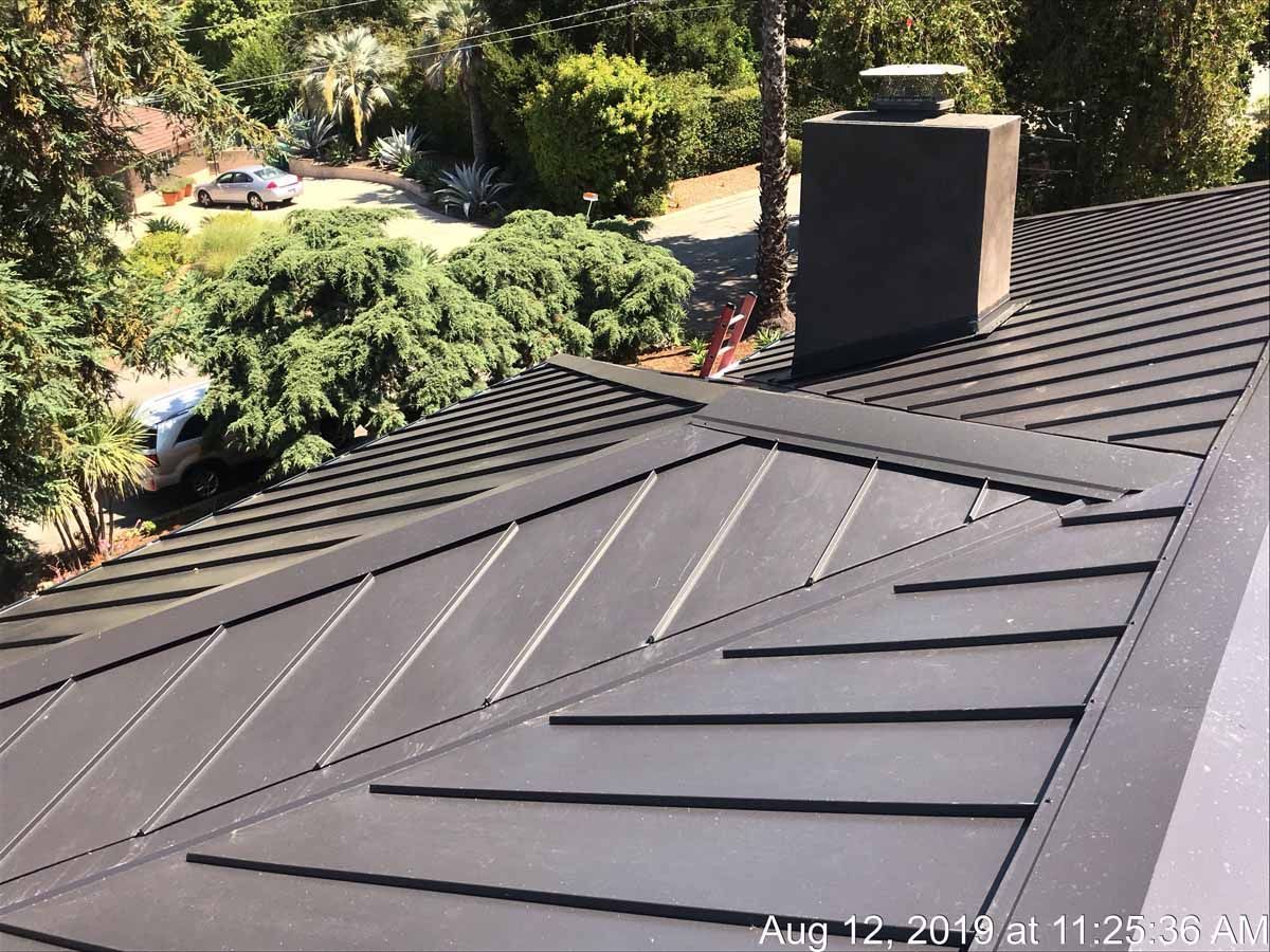 Dark gray metal roof with chimney, surrounded by trees and greenery