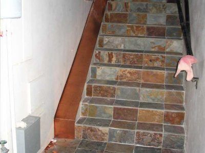 Steep tiled staircase with a pink handrail along the right side in a narrow hallway.