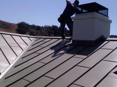 Person working on a metal rooftop beside a white chimney under a clear sky