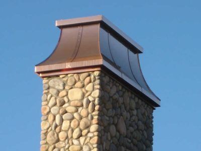 Stone chimney with copper cap against a blue sky