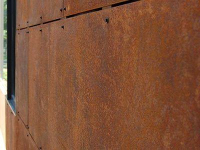 Rusty corrugated metal wall with visible rivets and a narrow window edge on the left