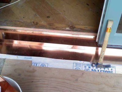 Open floor framing with copper pipes and a blue tool or beam at right side