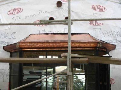 Construction scaffolding in front of a building with a copper-colored roof trim
