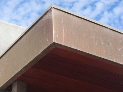 Close-up of a brown metal roof edge against a blue sky and white wall
