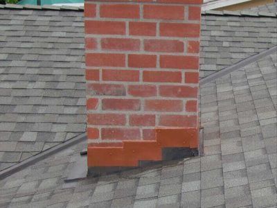 Brick chimney on a gray shingled roof with a dark flashing base.