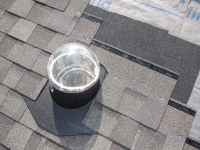 Roof vent pipe with a shiny metal cap on gray asphalt shingles.