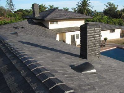 Dark shingled rooftop with skylight and chimney beside a swimming pool and house exterior.