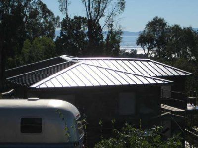 House with silver metal roof among trees, with water visible in the distance