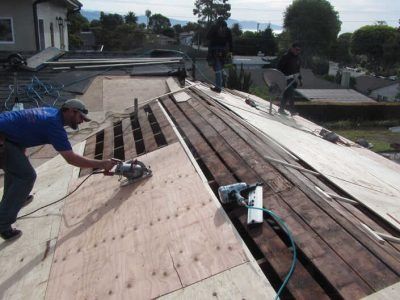 Worker repairing a roof with a power saw on a partly stripped rooftop