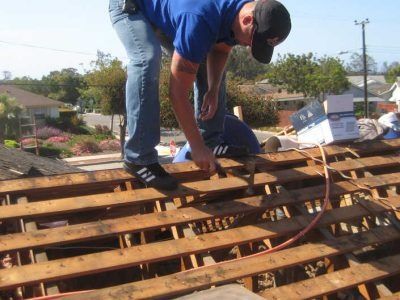 Worker kneeling on a rooftop, repairing wooden beams with a hammer.