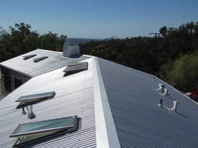 Metal roof with skylights and vents on a building beside trees under a bright sky