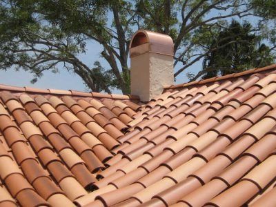Terracotta tile roof with a chimney against trees and blue sky