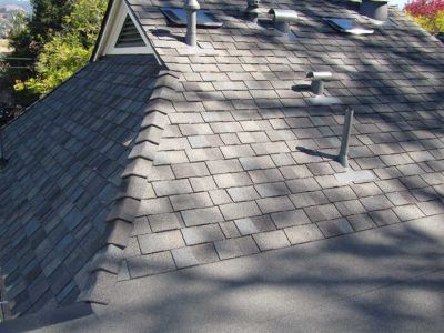 Gray shingled roof with two vent pipes and tree shadows in sunlight
