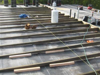 Workers installing materials on a stepped outdoor surface with lumber, tools, and cables.