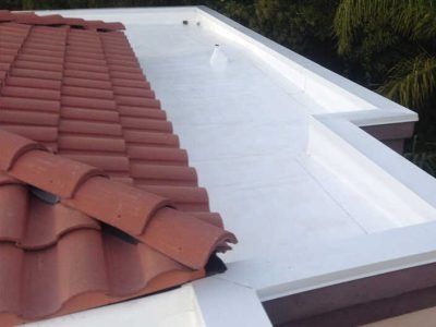Red tile roof beside a white flat roof with a roof edge and dark trees in the background