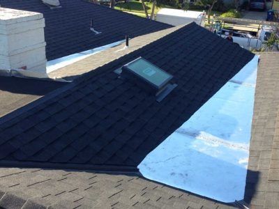 Rooftop with dark shingles, a skylight, and a large reflective patch of metal or tarp
