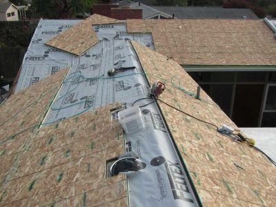 Roofers installing underlayment on a house roof with plywood sheathing exposed and a partially covered ridge