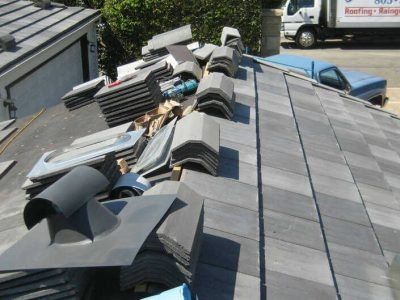 Roofer’s materials and torn shingles scattered across a gray roof, with a truck nearby