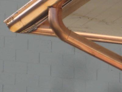 Copper gutter and downspout on the corner of a house roof against a gray wall