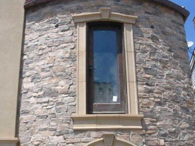 Tall narrow window set in a rounded stone wall with a tan trim and ledge