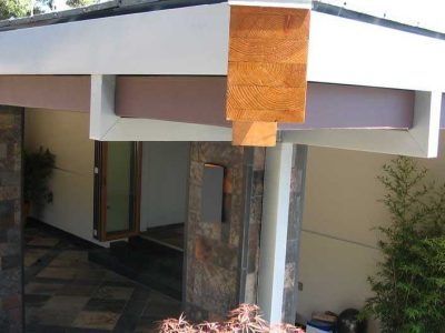 Modern house entrance with a white overhang, wooden column, and shaded patio walkway
