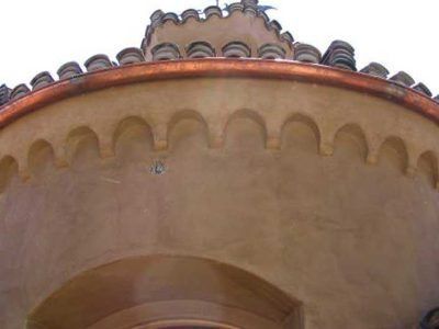 Round tan stucco tower with terracotta roof tiles and arched decorative trim