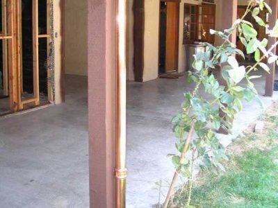 Covered porch with wooden posts and a leafy plant beside a concrete patio and grass area