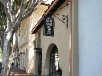 Street view of a beige storefront with an arched doorway and hanging sign under large trees