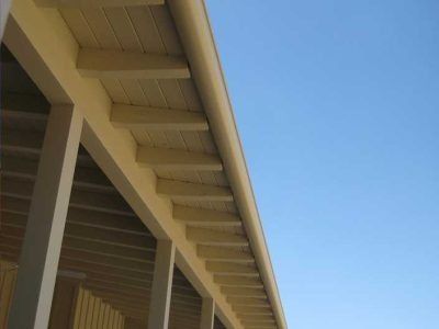 Beige house eaves and support beams against a clear blue sky