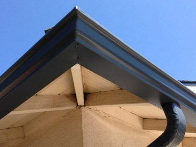 Close-up of a house roof corner with a black gutter and beige soffit against a blue sky