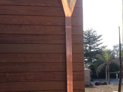 Wooden wall and roof corner with a decorative vertical beam, outdoors near a garden path.