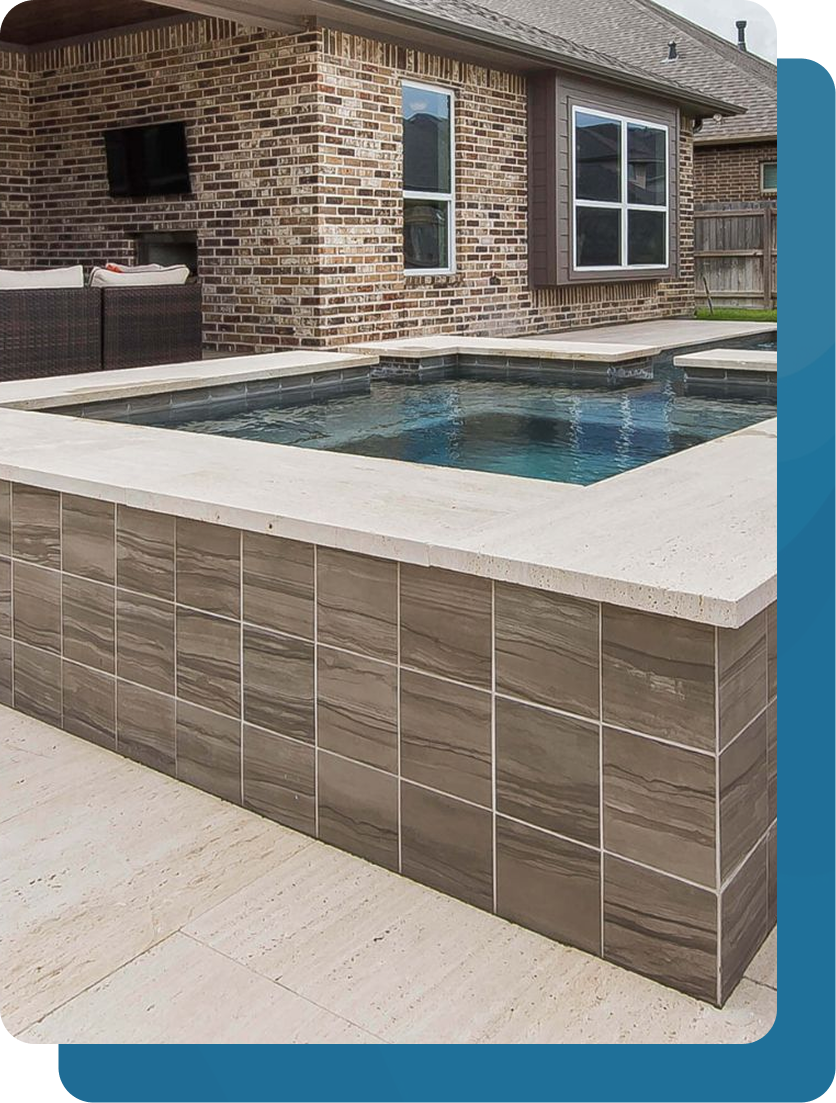 A backyard pool with brown tile surround. Brick wall with windows in the background.
