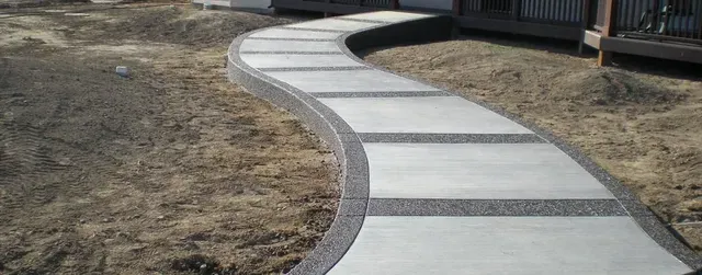 A curved concrete walkway leading to a deck in a backyard.