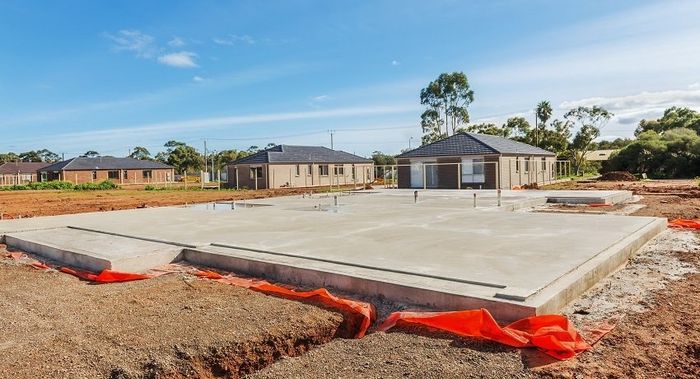 A house is being built on a dirt lot with a concrete foundation.