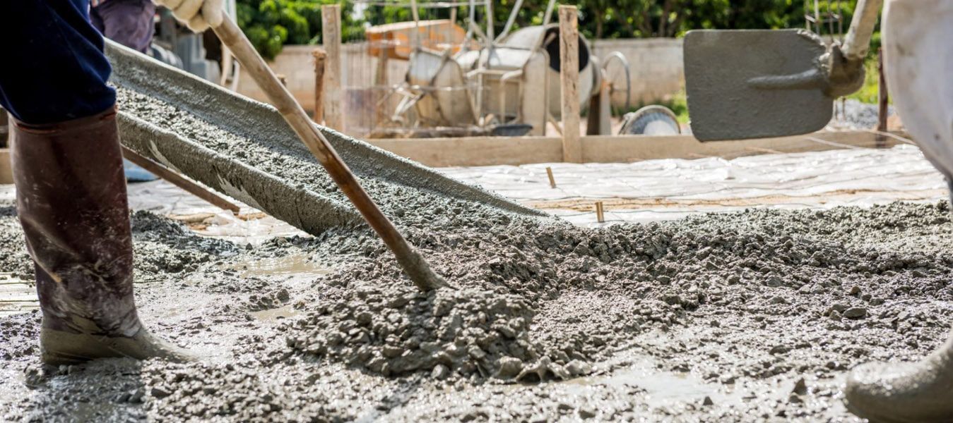 A person is pouring concrete into a hole with a shovel.