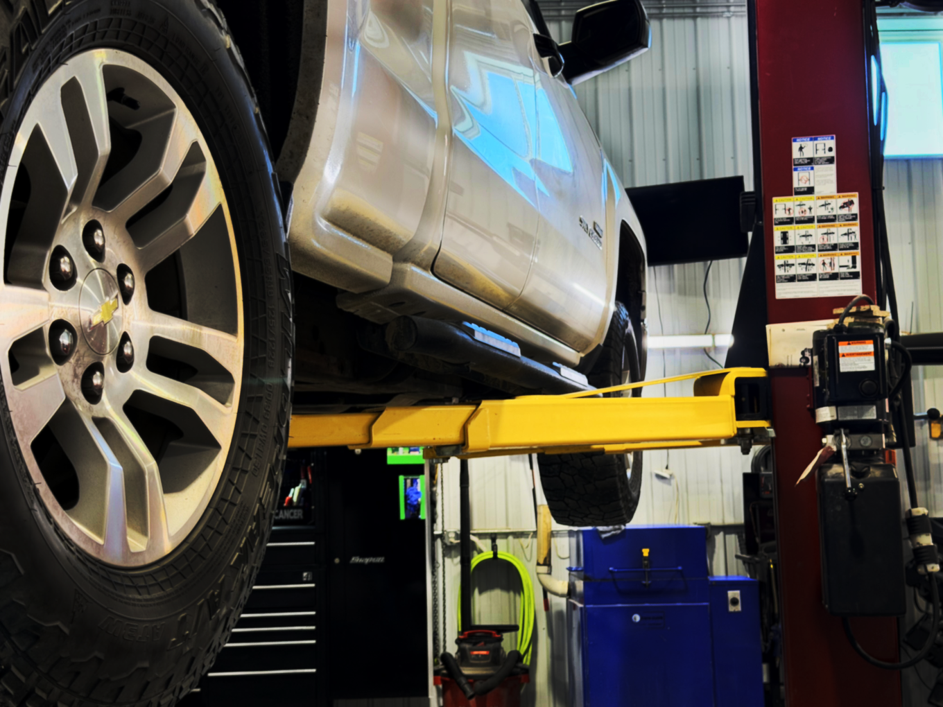 A silver truck on a yellow lift inside a garage, with a close-up of the front wheel.