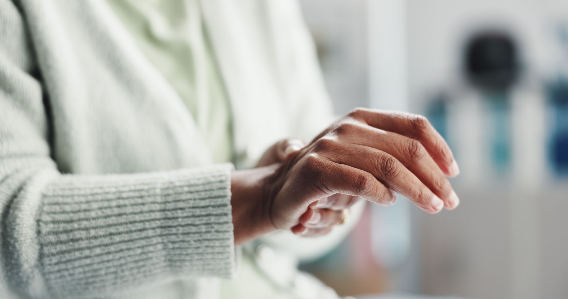 Person in a light green sweater, examining their wrist.