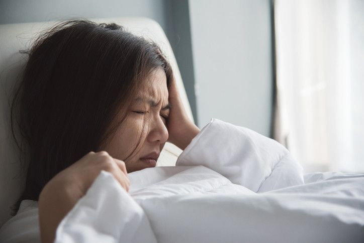 A woman is laying in bed with a headache.
