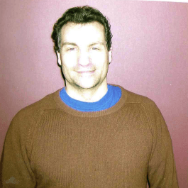 A man wearing a brown sweater and a blue shirt