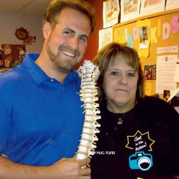 A man in a blue shirt holds a model of a spine next to a woman in a black shirt that says hug fund